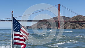 Views of a section of Golden Gate Bridge with northern tower and an American flag flattering in the wind