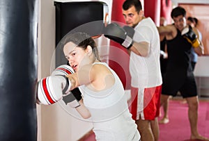 Vigorous sportswoman in the boxing hall practicing boxing punches with boxing bag