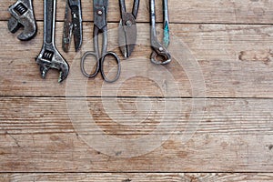 Viiew of vintage rusted tools on old wooden table: pliers, pipe wrench, screwdriver, hammer, metal shears, saws and other.