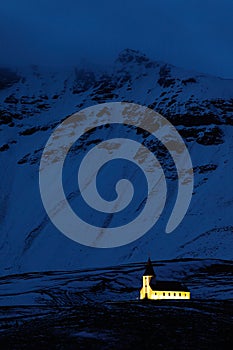 Vik Church in Iceland. Night photo with light church and dark blue snowy mountain. Winter scene from cold Iceland. Wild nature wit