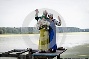 Viking family on a pier on a lake. a man, woman, and teenage girl wave their hands in greeting.