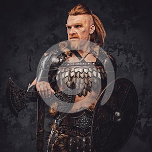 Viking posing with shield and axe against dark background