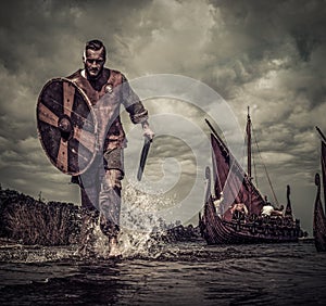 Viking warrior in attack, running along the shore with Drakkar on background