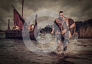 Viking warrior in the attack, running along the shore with Drakkar on the background.