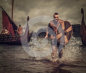 Viking warrior in the attack, running along the shore with Drakkar on the background.