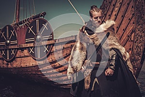 Viking warrior with sword standing near Drakkar on the seashore.