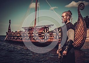 Viking warrior with sword standing near Drakkar on the seashore.