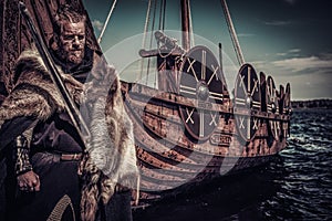 Viking warrior with sword standing near Drakkar on seashore