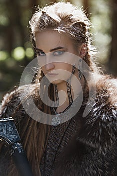 Viking woman with hammer wearing traditional warrior clothes in a deep mysterious forest.