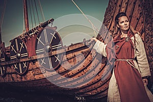 Viking woman standing near Drakkar on the seashore.