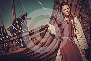 Viking woman standing near Drakkar on the seashore.