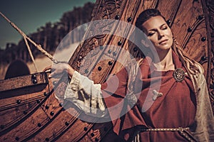 Viking woman standing near Drakkar on the seashore.