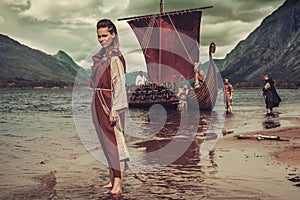 Viking woman standing near Drakkar on seashore photo