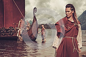 Viking woman standing near Drakkar on seashore photo