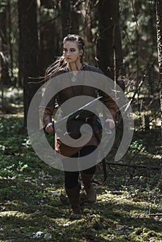 Viking woman with sword and hammer wearing traditional warrior clothes in a deep mysterious forest.