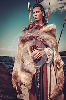 Viking woman with sword and shield standing on Drakkar.