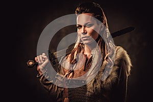 Viking woman with sword in a traditional warrior clothes, posing on a dark background.