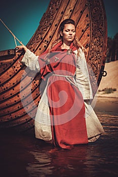 Viking woman in traditional clothes near drakkar