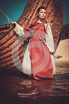 Viking woman in traditional clothes near drakkar