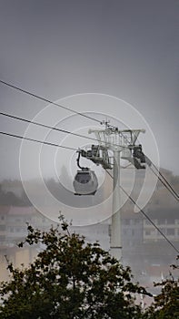 A Vilanova de Gaia cable car gondola suspended on hanging steel cables ascending under a cloudy sky with the classic Gaia photo