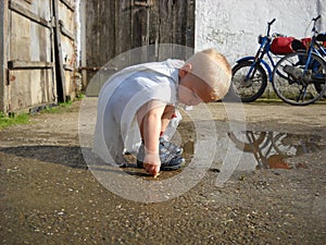 Village boy playing in a dirty puddle next to a barn in a grandmothers yard