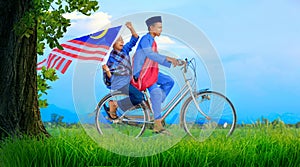 Village boy riding old bicycle at paddy field holding a Malaysian flag celebrating Independence Day