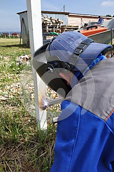 In the village on the construction site, a welder welds a fence