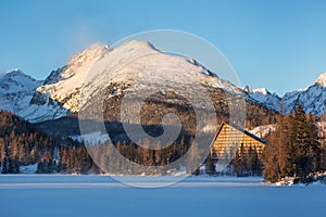 Winter view of the Strbske pleso village with hotel, coniferous forest and snowy peaks.