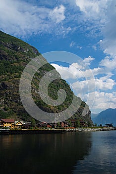 Village in Flam, Norway. Country houses at sea shore on mountain landscape. Fjord and mountains on cloudy sky. Vacation