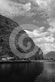 Village in Flam, Norway. Country houses at sea shore on mountain landscape. Fjord and mountains on cloudy sky. Vacation