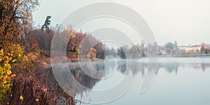 The village is in a fog. Panoramic view of morning haze over surface of the lake near Gatchina city