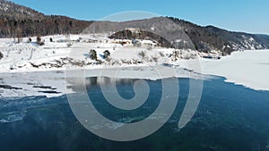 A village at the foot of mountains. Cars drive along the road on the lake shore