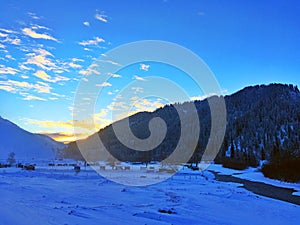 Village by Frozen River at Winter Sunrise