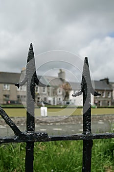 Village green and terraced houses through black metal fence