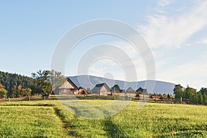 Village houses on hills with green meadows in summer day. House of shepherds in mountains in carpathian