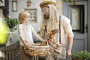 Village life. Country boy with Daddy brown chicken and a big basket in the yard near the front door.Summer day