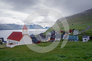 Village of Mikladalur in Kalsoy, Faroe Island. White wooden church with fjord and village in the background photo