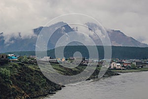 Village near river on background forested mountain in fog and cloud.