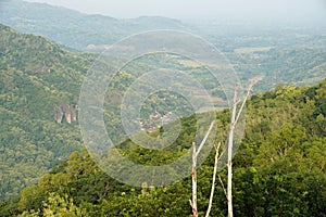 A village nestled at the base of a verdant hill, dotted with large rock formations that cling to the slope.