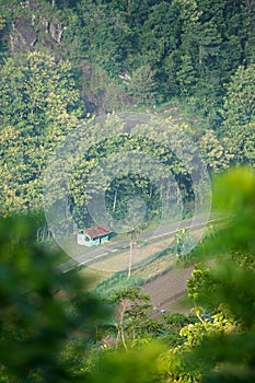 A village nestled at the base of a verdant hill, dotted with large rock formations that cling to the slope.