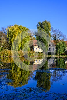 Village pond with reflections of colorful trees in the water and an old mano