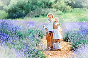 Village scene with children in vintage clothes in the middle of a lavender field. Boy in white hat, shirt and brown trousers hug