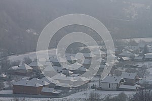 The village is shrouded in winter fog in the river valley between the Carpathian mountains.