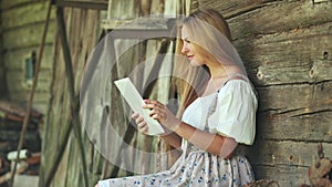 Village Slavic girl flipping a tablet in the countryside by the barn.