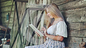 Village Slavic girl flipping a tablet in the countryside by the barn.