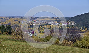 The village among the Ural fields and forests in autumn decoration. In the foothills of the Western Urals, golden autumn.