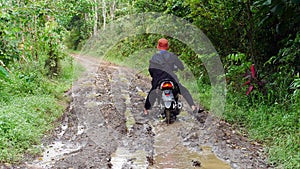 A villager rides a motorbike through a muddy forest road
