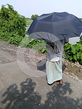 a villager with umbrella wathing his farm in the sun