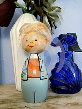 Vimtage Wooden Figurine of a Boy in a Blue Suite and Orange Vest, Holding a Flower, and a Blue Glass Perfume Bottle