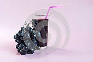 A vine with black berries and a transparent glass with grape juice.